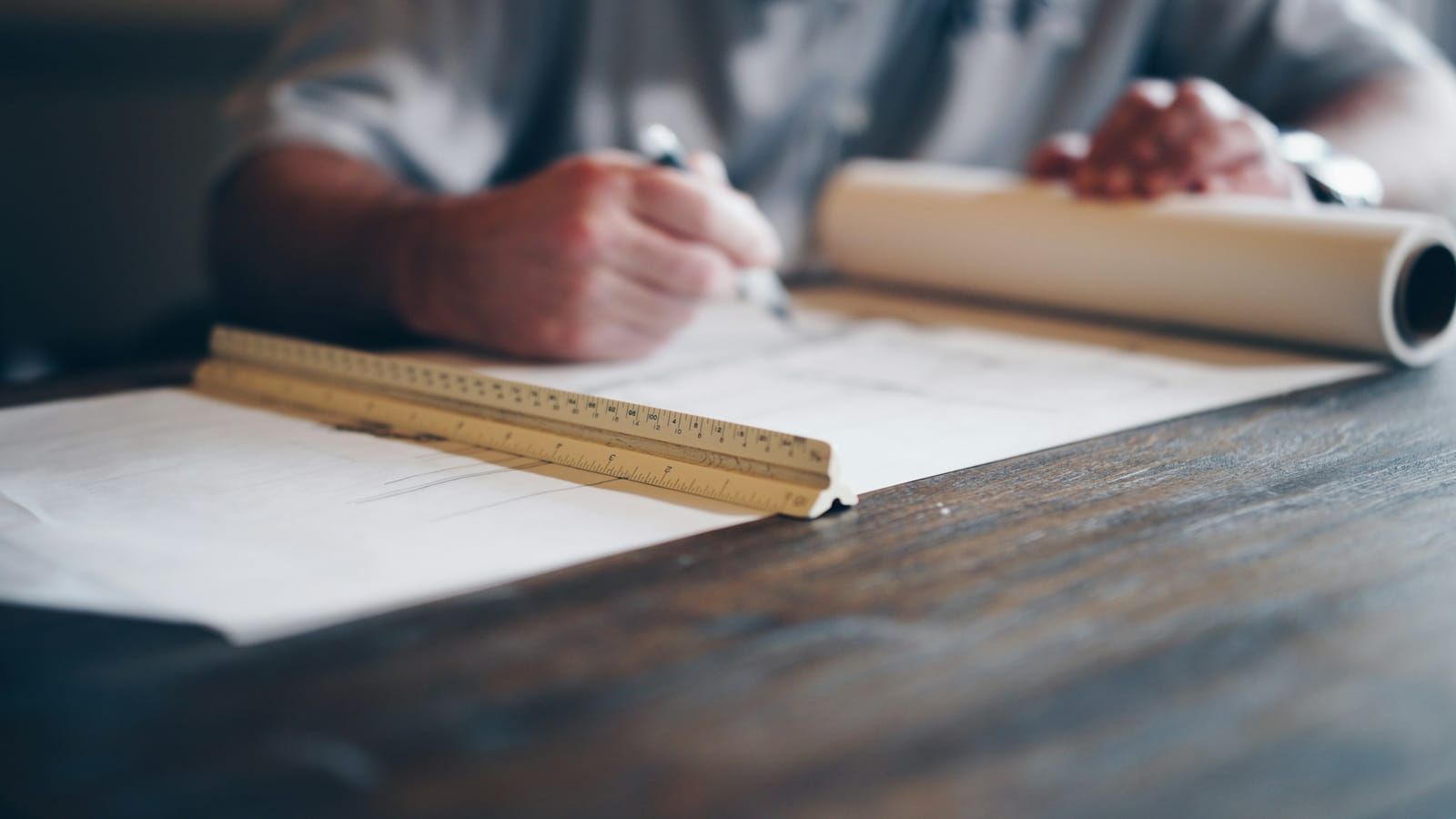 A person drafting on a blueprint with a ruler at a desk
